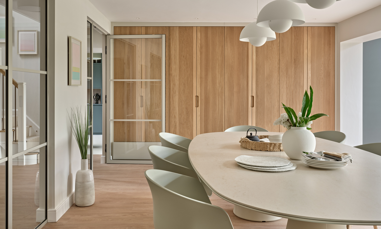 Modern oval dining table with light green chairs contemporary pendants and bespoke fluted oak fitted joinery